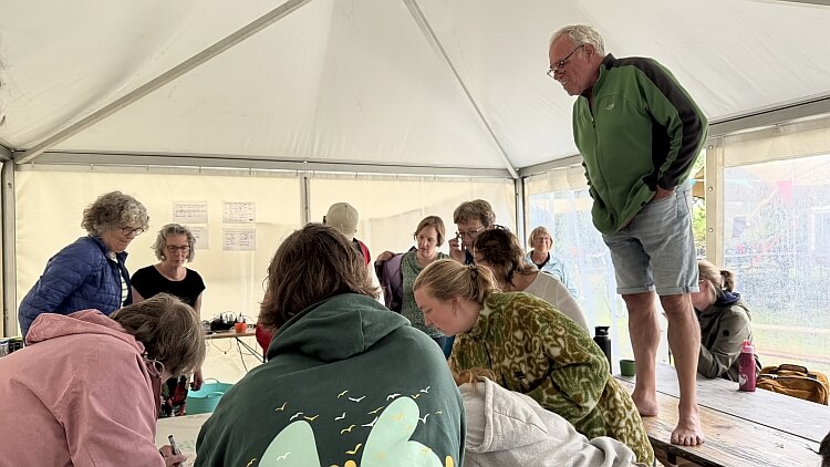 Feije klimt op de tafel om het werk van de deelnemers aan de workshop van bovenaf te bekijken.